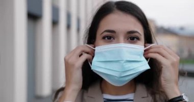 Açık havada dikilen ve yüzüne tıbbi maske takan mutlu beyaz kadın portresi. Sokakta maske takmış güzel, koyu saçlı bir kadın. Koruyucu önlemler. Virüs ve karantina kavramı