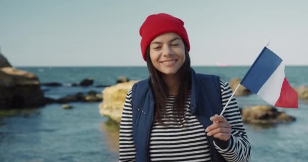 Schöne Touristin, Austauschstudentin, Frankreich-Fahne in der Hand, lächelnd in die Kamera blickend, am Meer stehend. — Stockvideo