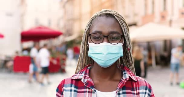 Ritratto di giovane donna afroamericana bella in maschera medica e occhiali in piedi in strada e guardando la macchina fotografica. Concetto pandemico. Primo piano del viso femminile nella protezione respiratoria. Quarantena — Video Stock