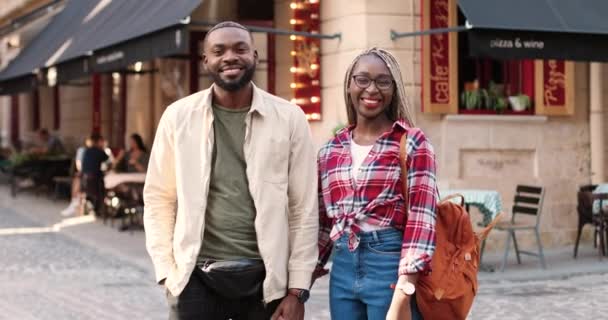 Porträtt av unga glada afroamerikanska par stående utomhus i staden hand i hand och tittar på kameran. Manliga och kvinnliga touister ler och poserar för kameran i stan. Dolly sköt. Zooma in. — Stockvideo