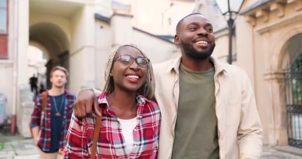 Glada glada unga afroamerikanska par i kramar går på gatan, skrattar och har kul. Manliga och kvinnliga turister omfamnar och strosar i antika staden med fin gammal arkitektur. — Stockvideo