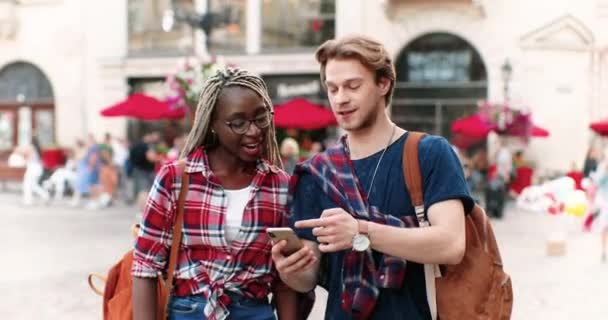 Casal de raças mistas ou amigos masculinos e femininos andando na rua da cidade e olhando para o telefone celular. Jovem multi homem étnico e mulher usando smartphone e conversando. — Vídeo de Stock