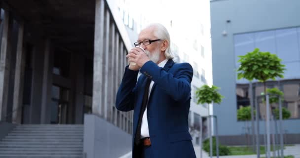 Viejo caucásico en gafas hablando por teléfono móvil afuera y bebiendo. Hombre de negocios jubilado y rico hablando por celular y tomando café en la calle de la ciudad. Conversación. Charla de negocios. — Vídeos de Stock