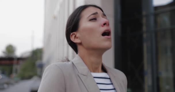 Portrait of beautiful Caucasian woman runny nose walking in city on street with tablet in hand and covering face with tissue. Close up of sick unwell young female sneezing and coughing. Virus concept — Stock Video
