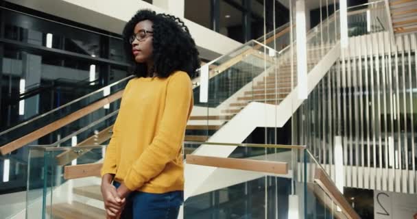 Portrét mladé krásné africké americké studentky ve žlutém svetru s kudrnatými vlasy stojící v knihovně lobby při pohledu na kameru usmívající. — Stock video