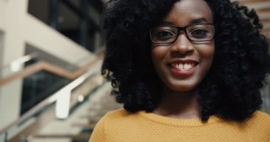 Sarı kazaklı, kıvırcık saçlı ve kütüphane lobisinde kameraya bakıp gülümseyen güzel Afro-Amerikan kadının portresini yakından çek..