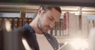 Kütüphanede rafların arasında dikilip kitap okuyan yakışıklı, zeki, beyaz bir adama yaklaş..