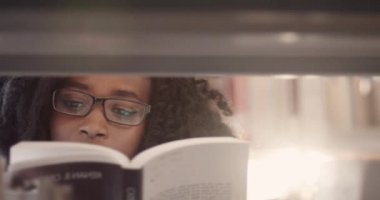 Kütüphanede rafların arasında duran ve dikkatle kitap okuyan güzel, zeki, Afro-Amerikan kadınına yaklaş..