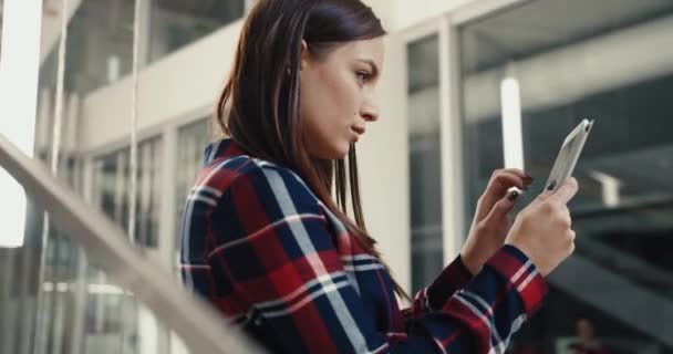 Νεαρή όμορφη φοιτήτρια στέκεται στο λόμπι του πανεπιστημίου και δακτυλογράφηση θέση για τα κοινωνικά δίκτυα χρησιμοποιώντας tablet. — Αρχείο Βίντεο