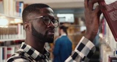 Kütüphanede dikilen zeki Afro-Amerikan erkek öğrenciye yakın çekim yapıp kitabı raftan indiriyor ve okumaya başlıyor..
