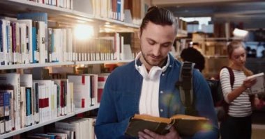 Kütüphanede duran kot gömlekli genç öğrencinin portresi kitap okuyor ve kameraya gülümsüyor..
