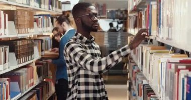 Ekose gömlekli, gözlüklü genç bir Afro-Amerikalı kütüphanede dolaşıyor ve okumak için kitap topluyor. Öğrenci sınava hazırlanıyor..