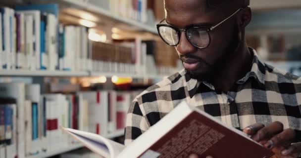 Nahaufnahme einer jungen intelligenten afroamerikanischen Studentin, die in der Bibliothek steht und in Vorbereitung auf Prüfungen eifrig Bücher liest. — Stockvideo