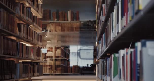 Universiteitsbibliotheek in avondtijd. Jonge mannelijke student loopt door de boekenplanken en leest intensief boek. Afstandsonderwijs. — Stockvideo