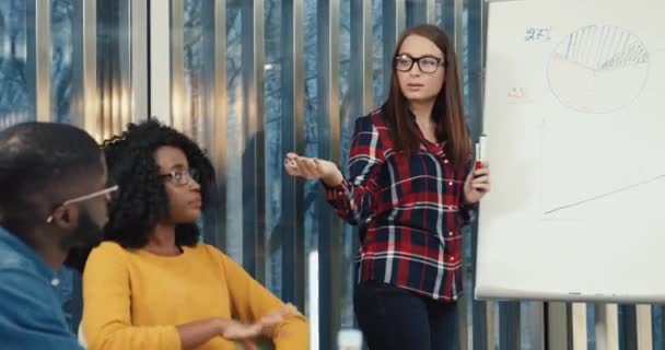 Joven inteligente hermosa maestra con gafas ayuda a los estudiantes a entender el tema de la conferencia y escribe información a bordo. — Vídeos de Stock