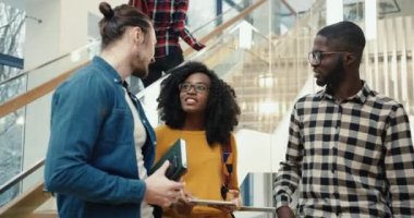 Üç çok uluslu öğrenci tatil boyunca üniversite salonunda durup dersler hakkında konuşuyor ve boş zamanlarını eğlenerek geçiriyorlar..