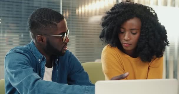 Blisko dwóch młodych afrykańskich studentów: chłopak i dziewczyna siedzący razem i przygotowujący się do egzaminów patrzących na ekran laptopa. — Wideo stockowe