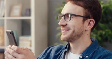 Mutlu bir adam evinde kanepede oturuyor ve boş zamanlarını akıllı telefonuyla sosyal ağlarda arkadaşlarıyla mesajlaşarak geçiriyor..