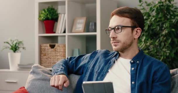 Porträtt av manliga nöjda trådlösa surfplatta användare i glasögon sitter hemma och tittar på kameran ler. — Stockvideo