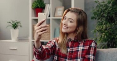 Genç, sarışın, güzel bir kız. Sosyal ağ kurmak için selfie çekiyor. Kanepede tek başına otururken..
