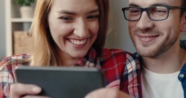 Evlerinde kanepede oturup telefonda komik videolar izleyen genç ve güzel çifti yakından çek..