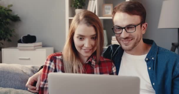 Close up de jovem casal caucasiano assistindo comédia no laptop enquanto sentado em casa no sofá. — Vídeo de Stock