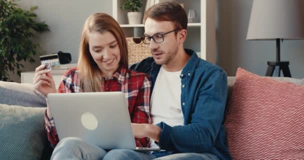 Nahaufnahme eines jungen glücklichen Paares, das zu Hause auf dem Sofa sitzt und mit Laptop erfolgreich online einkauft. — Stockvideo