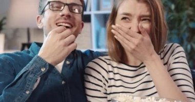 Genç evli çiftin TV 'de komedi izlerken yüksek sesle kahkaha atması ve patlamış mısır yemesi..