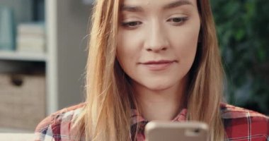 Genç ve güzel sarışın kadının sosyal ağlarda akıllı telefon kullanarak arkadaşlarıyla sohbet edişini yakından çek. Mutlu kız telefona bakıp gülümsüyor..