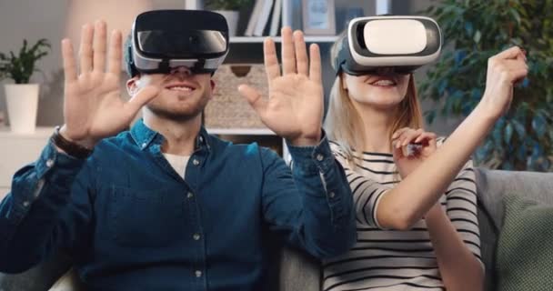 Close-up van jong getrouwd stel zitten thuis op de bank en het spelen van spel in virtual reality bril hebben plezier. — Stockvideo