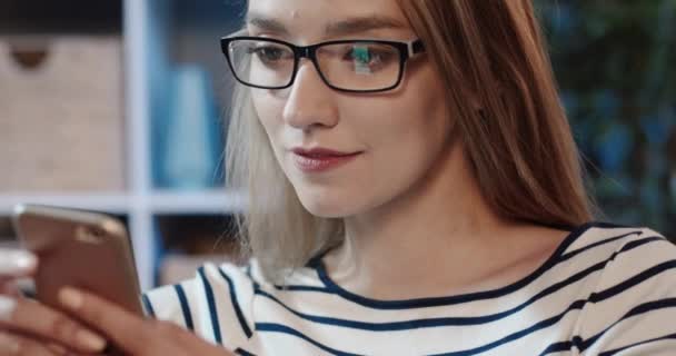 Primer plano de la joven hermosa mujer en gafas de pasar tiempo libre en las redes sociales utilizando el teléfono inteligente y oliendo con chistes. — Vídeo de stock