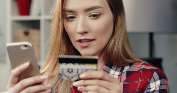 接近年轻漂亮的金发姑娘，在智能手机屏幕上检查银行卡，看是否中了彩票。女人在计划去哪里花钱. — 图库视频影像
