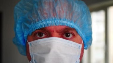 Tıbbi tek kullanımlık yüz maskesi ve mavi tek kullanımlık tıbbi önlük giyen yorgun profesyonel doktor. Tıbbi prosedürler sırasında sağlık uzmanı. Kişisel koruma ekipmanları 