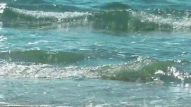 Rüzgar dalgalar yaratır. Mavi denizin kumlu kıyısı kabarcıklar oluşturur. Güneşin doğuşunda berrak masmavi deniz suyu. Yaz güneşinde deniz manzaralı güzel bir arka plan. Cennet doğası