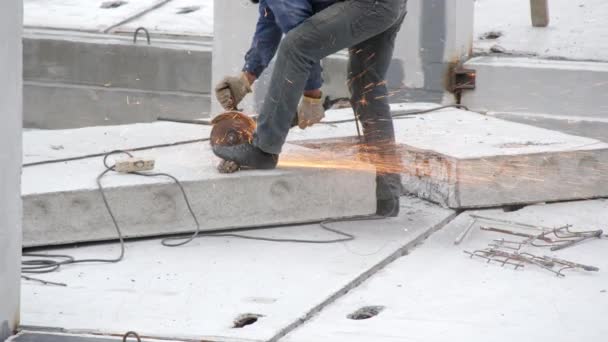 専門のビルダーは 建設現場で強化コンクリートスラブ上の角度研削盤と鉄のリバーをカットします 火花が電気の円形ののこぎりから飛びます 新しい建物の建設 — ストック動画