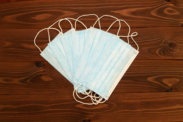 Blue surgical 3-ply disposable protective medical face masks with rubber ear straps to cover the mouth and nose on a brown wooden background. Objects are fan-shaped. Health care supplies. Close-Up