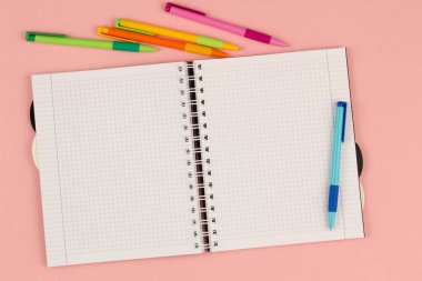 Pembe arka planda açık okul karesi defter. Kağıt kitap boş beyaz sayfa ve çalışma kalemi masanın üzerinde. Ofis malzemeleri ve masaüstü not defteri. Okula dönelim. Uzayı metin için kopyala. Üst görünüm