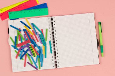 Açık okul karesi defter, kalem, cetvel, pembe arka planda renkli matematik sopaları. Masanın üzerinde boş beyaz bir sayfa kağıt var. Ofis malzemeleri masaüstünde. Uzayı metin için kopyala. Üst görünüm