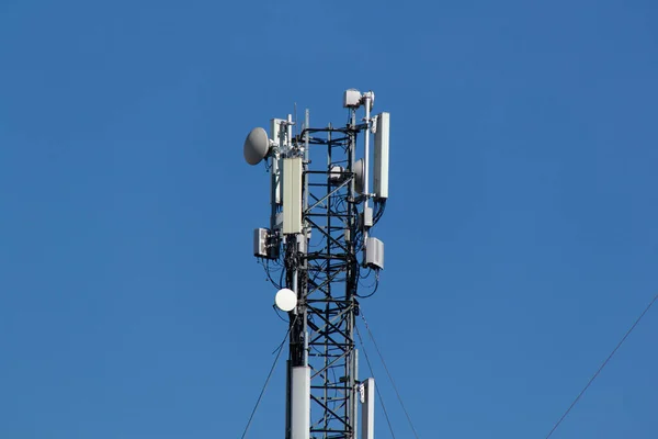 Mobile cell phone tower against the background of a blue sky and white cloud. Telecommunication TV tower. Cellular antenna. Wi-fi transmitter and receiver module.