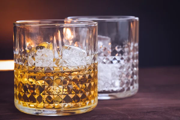 Dos vasos de whisky con cubitos de hielo en la mesa de madera, ambiente cálido — Foto de Stock