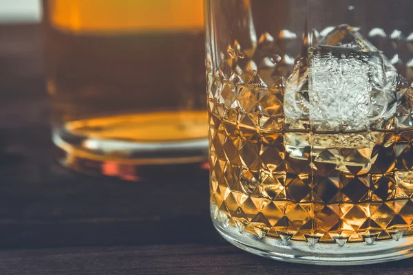 Vaso de whisky con cubitos de hielo cerca de la botella en la mesa de madera, ambiente cálido — Foto de Stock
