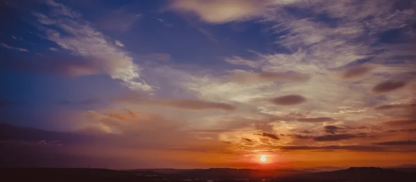 Sunset scene with sun fall and ray light, clouds in background, warm colorful sky — Stock Photo, Image