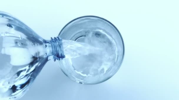 Füllen eines Glases mit Wasser durch Flasche auf weißem Hintergrund, Ansicht oben, Ernährungskonzept