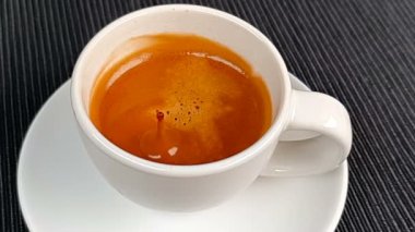 Kahve damlası, siyah arka planda köpük, yiyecek ve içecekle birlikte espresso İtalya kahvesinin içinde süper yavaş çekimde düşüyor.