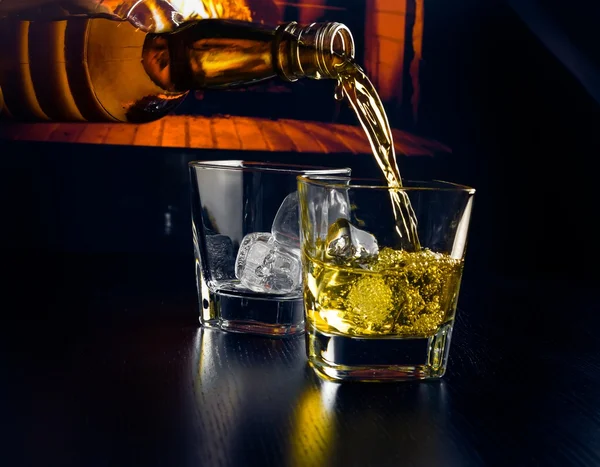 Man hälla glas whiskey med isbitar framför den öppna spisen — Stockfoto