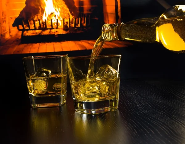 Hombre vertiendo dos vasos de whisky con cubitos de hielo en frente de la chimenea — Foto de Stock