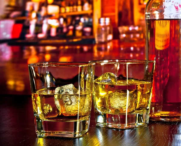 Glas whiskey med is på bar bord nära whiskey flaska på varm atmosfär — Stockfoto