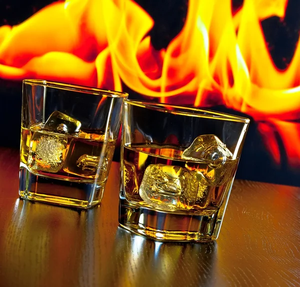 two glasses of whiskey with ice cubes in front of the flame