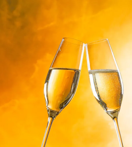 A pair of champagne flutes with golden bubbles on golden light background — Stock Photo, Image