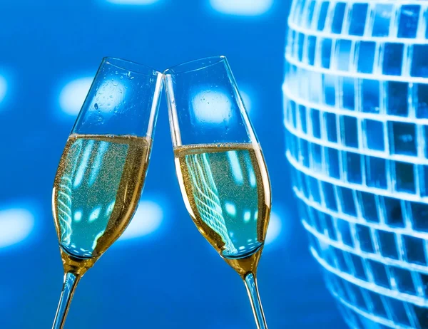 Dvojice šampaňské flétny zlaté bubliny, aby na zdraví na zářivě modré disco koule pozadí — Stock fotografie